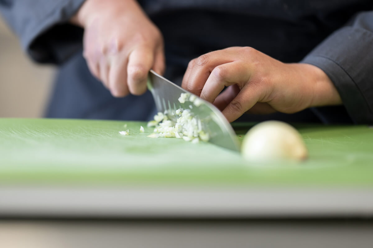 Hände schneiden eine Zwiebel auf einem grünen Schneidebrett mit einem großen Küchenmesser