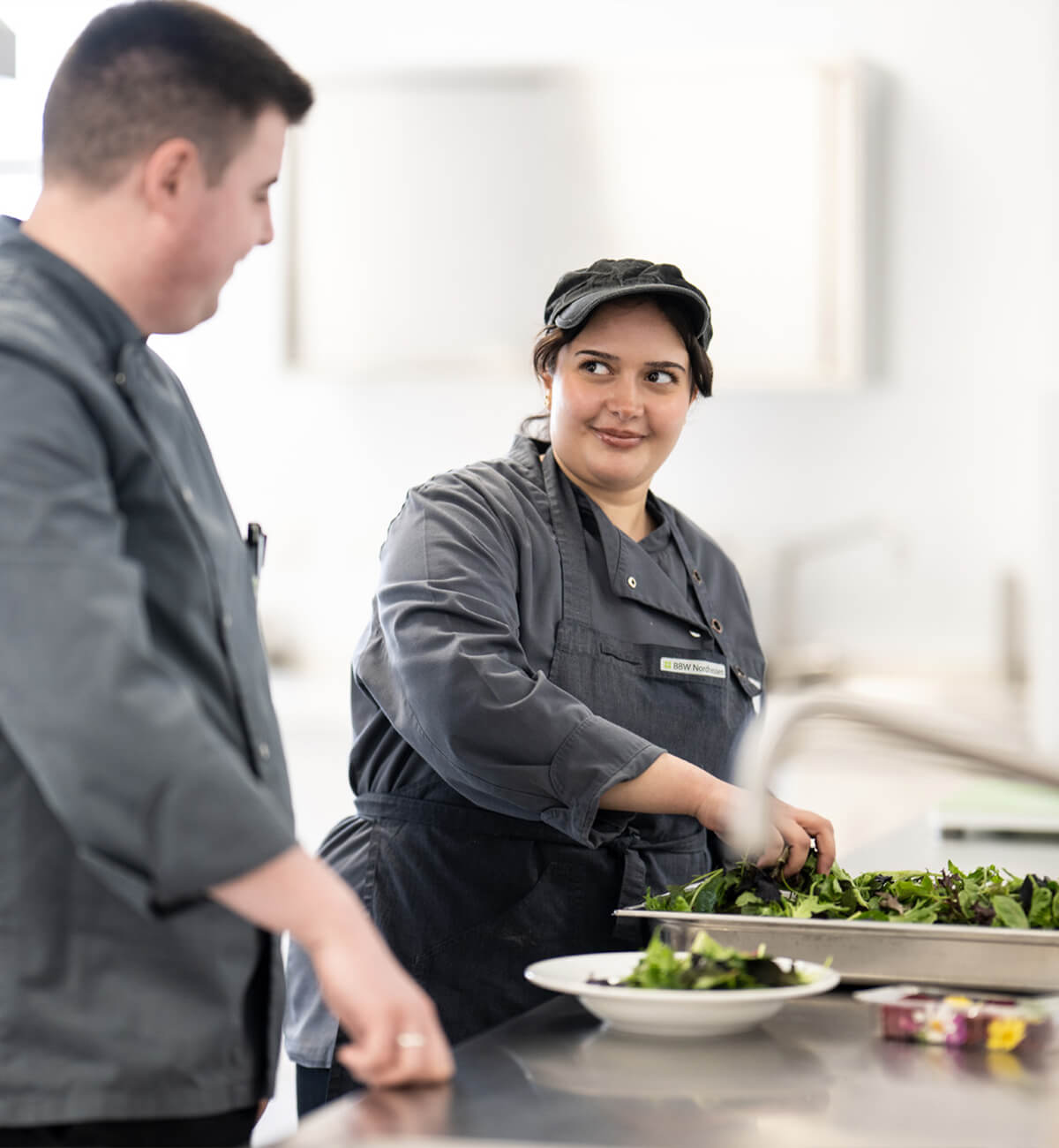 Zwei Köche in grauen Kochjacken bereiten gemeinsam Salat in einer professionellen Küche zu