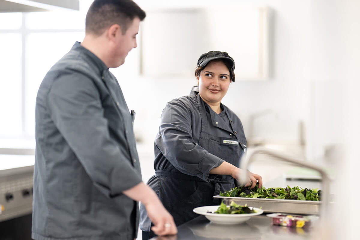 Zwei Köche in grauen Kochjacken bereiten gemeinsam Salat in einer professionellen Küche zu