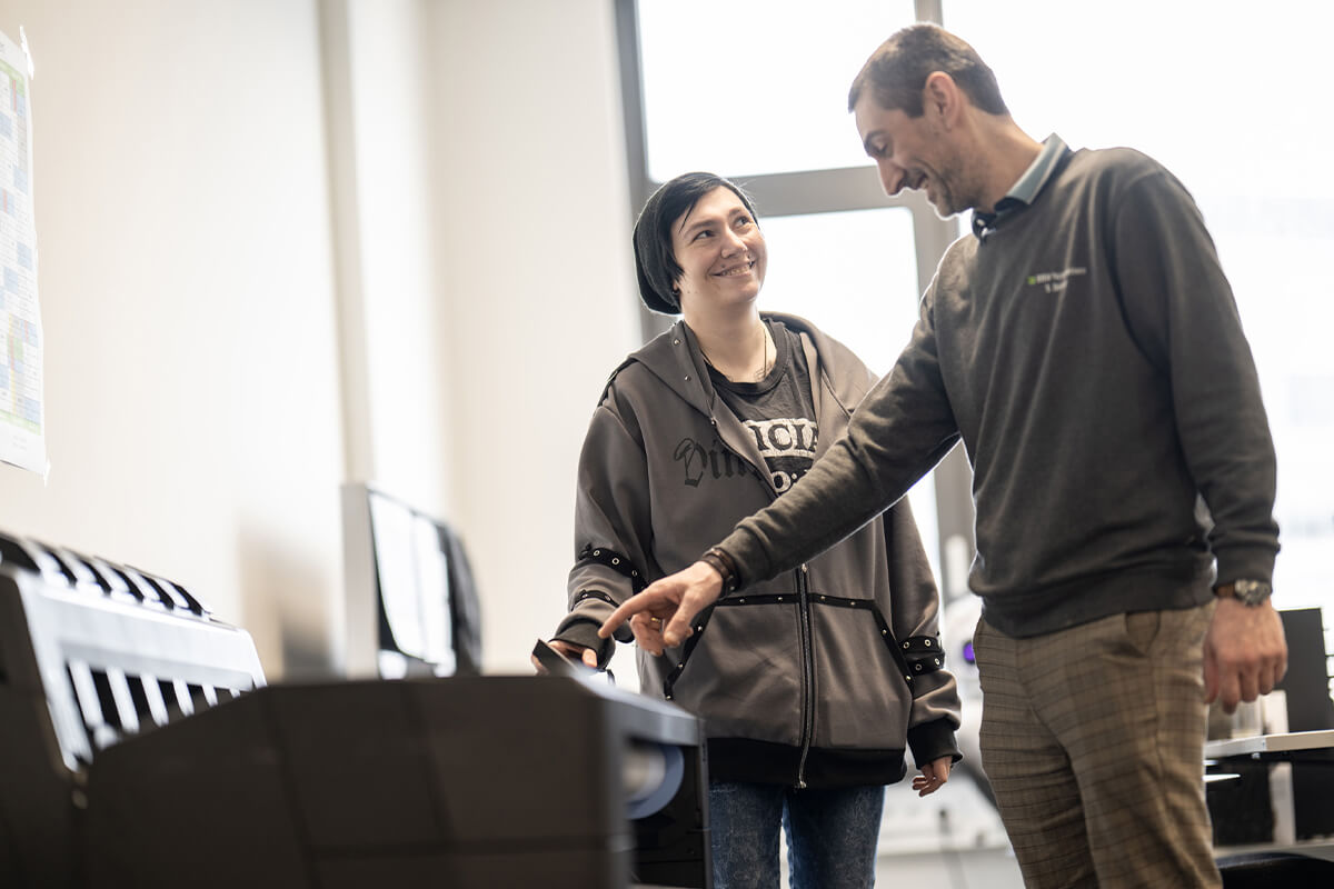 Zwei lächelnde Personen stehen gemeinsam vor einem Drucker