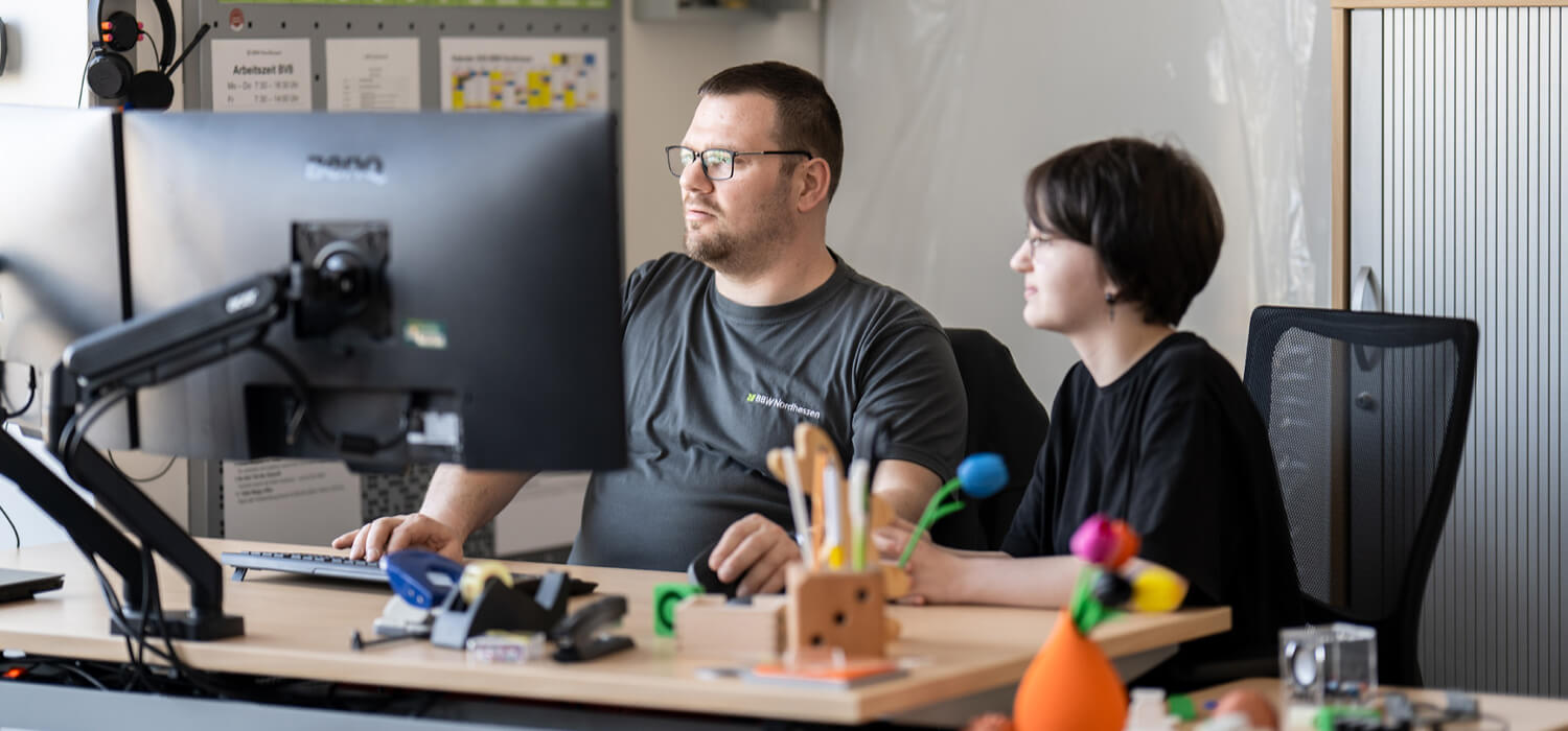 Zwei Personen sitzen gemeinsam an einem Tisch vor einem Computer
